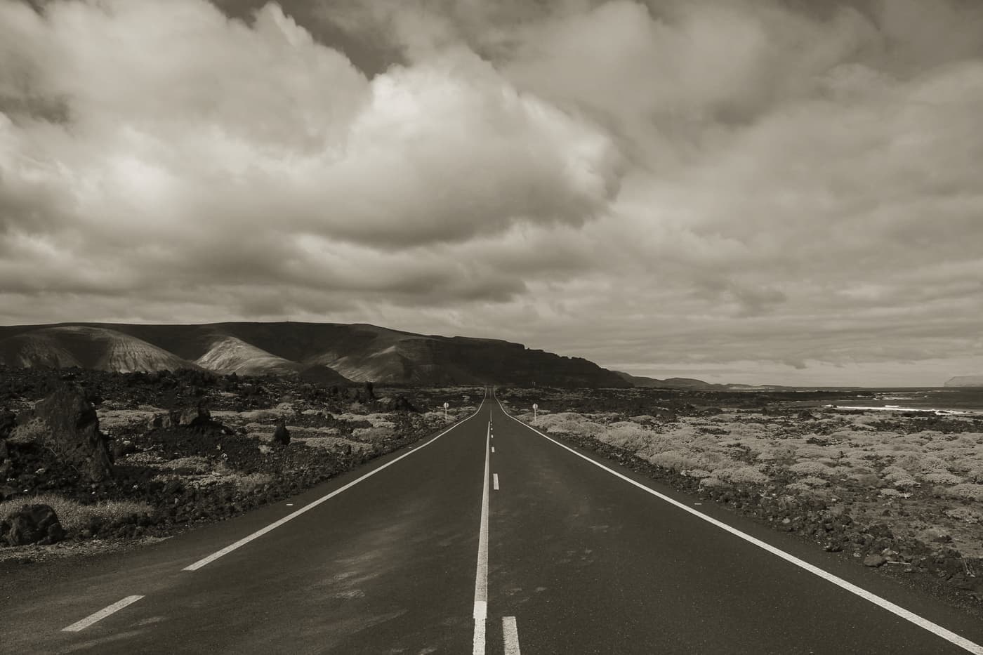 An empty two-lane road stretching toward low hills